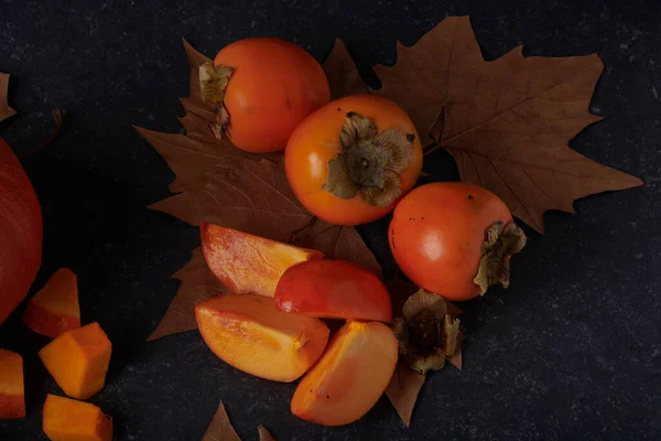 Kaki entier et tranché avec des feuilles d'automne marron sur un dessus en pierre — Photo