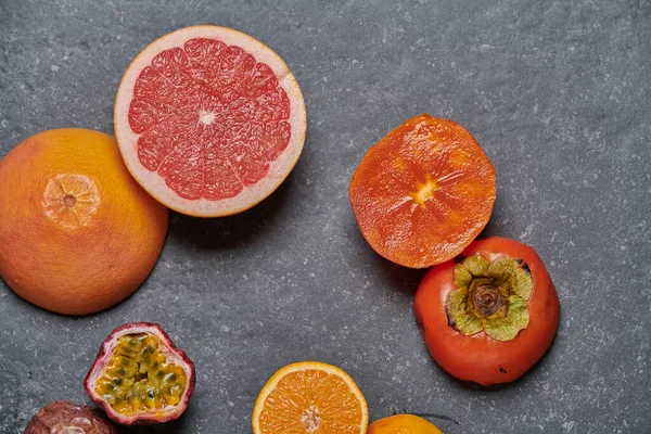 Top view of orange with grapefruit, pomegrade, passion fruit and kaki on dark grey background. Healthy and fresh fruits for boosting vitamin C and immunity system, top view.