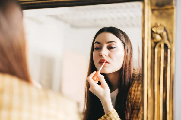 Young beautiful woman looking at mirror while doing makeup, applying lipstick. High quality photo