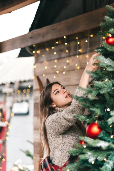 年轻的高加索女人穿着格子花 在一座木头房子的阳台上装饰着一棵圣诞树 高质量的照片 — 图库照片