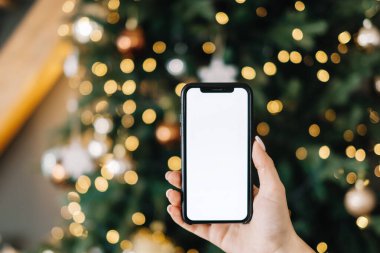 Beyaz ekranlı akıllı telefonu olan bir kadın Noel ağacının yanında evinde taklit yapıyor. Yüksek kalite fotoğraf