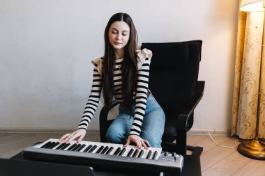 Genç bir kadın evde uzaktan bilgisayarla piyano çalmayı öğreniyor..