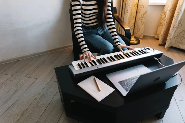 Young woman learns to play the piano keys using a laptop at home distantly.