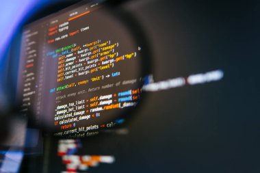 Bilgisayar ekranındaki program kodu büyüteçle. Yakın plan..