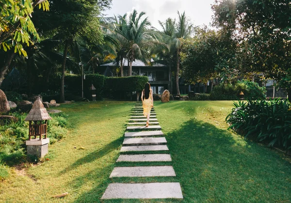 Mujer joven camina en un bosque tropical con hierba verde y palmeras. — Foto de Stock