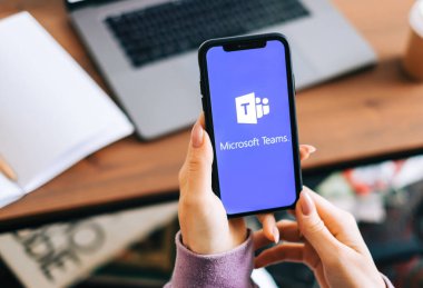 Microsoft Ekipleri video arama uygulaması logosuyla el ele tutuşan iPhone ekranda.