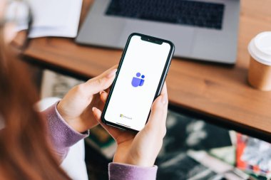 Microsoft Ekipleri video arama uygulaması logosuyla el ele tutuşan iPhone ekranda.