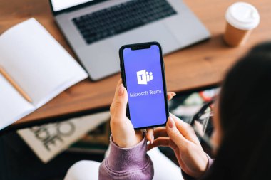 Microsoft Ekipleri video arama uygulaması logosuyla el ele tutuşan iPhone ekranda.