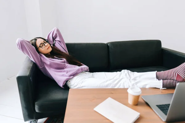 Young caucasian woman relaxing on a sofa in front laptop in living room after work.