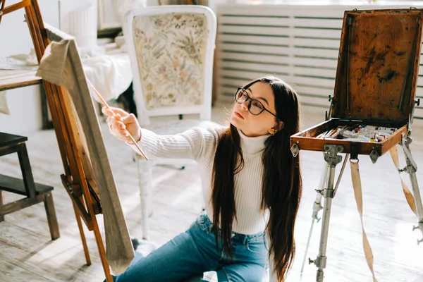 年轻的高加索女画家 坐在地板上 拿着画笔 在画布上画画 在一个家庭工作室里工作 — 图库照片