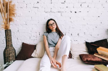 Gözlüklü çekici beyaz bir kadının otantik yaşam tarzı portresi. Evdeki kanepede oturuyor ve kameraya bakıyor..