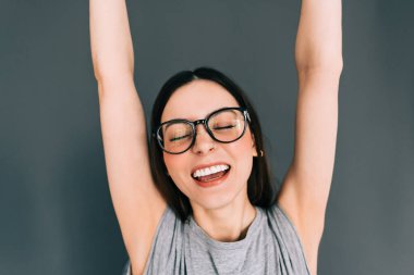 Gözlüklü neşeli beyaz kadın portresi. Gri arka plana el koyup kameraya bakıyor..