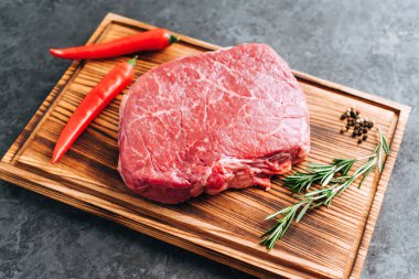 Tahtada çiğ biftek ve biberiye, biber ve baharatlı siyah arka plan.