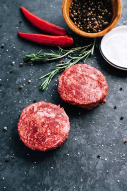 Siyah zemin üzerinde hamburgerler için taze kıymalı biftek, biberiye, biber ve baharatlı.