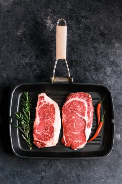 Çiğ pirzola ve New York bifteği, siyah ızgara tavada kırmızı biber ve biberiyeli..