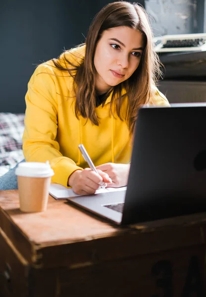 Young woman college student studying with laptop, distantly preparing for test exam, writing essay doing homework at home, distantly education concept