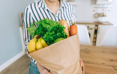 Beyaz kadın, modern mutfakta taze sebze ve baget ile birlikte eko alışveriş çantası tutuyor..