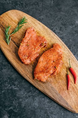 Marinated turkey steak on a wooden board with rosemary and chili pepper.	