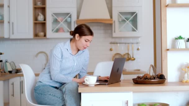 Ung smilende kaukasiske kvinde bruger bærbar computer på køkkenet, forbindelse til videochat møde med familie eller venner, vinke. – Stock-video