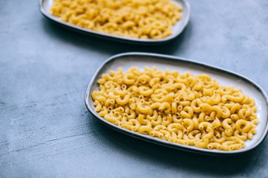 Wheat raw Italian pasta in plates isolated on blue background.	