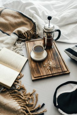 Yatakta açık bir kitap, kahve makinesinde demlenmiş ve tahta bir tahtanın üzerinde. Sabah evde, rahatlık ve rahatlık..