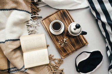 Yatakta açık bir kitap, kahve makinesinde demlenmiş ve tahta bir tahtanın üzerinde. Sabah evde, rahatlık ve rahatlık..