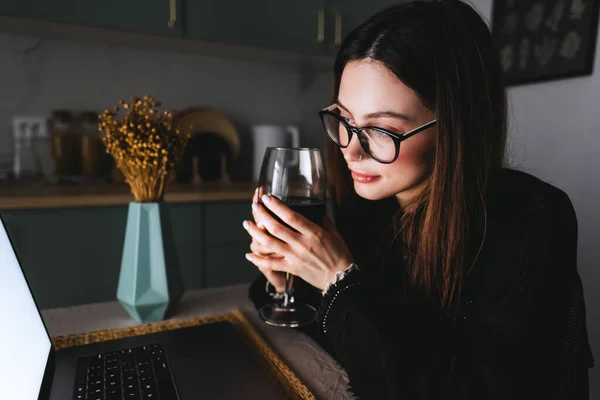 Young millennial woman having video call on laptop computer and drinking wine, use technology for communicate with friends or family.