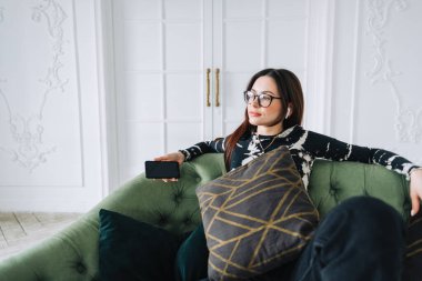 Kulaklıklı çekici beyaz kadın evdeki rahat koltukta dinleniyor ve müzik dinliyor.