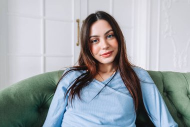 Çekici bir genç kadının portresi, gündelik giysiler içinde kanepede oturmuş kameraya bakıyor..