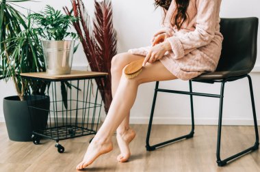 Ahşap fırça tutan ve ayaklarına kuru masaj yapan bir kadın. Kişisel bakım danışmanı.