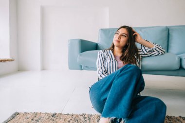 Genç, sakin, Kafkasyalı kadın dinleniyor, modern oturma odasındaki kanepenin yanında oturuyor, evde dinlenen tembel, mutlu kadın.