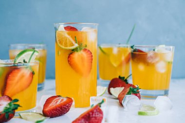 Farklı bardaklarda taze portakallı çilekli mojito buz küpleri ve masada limon dilimleri. Yaz ferahlatıcı içecek