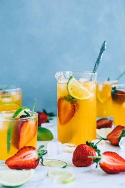 Farklı bardaklarda taze portakallı çilekli mojito buz küpleri ve masada limon dilimleri. Yaz ferahlatıcı içecek