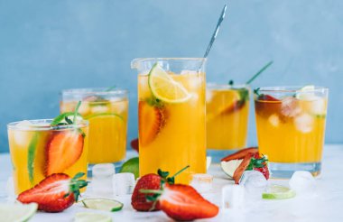 Farklı bardaklarda taze portakallı çilekli mojito buz küpleri ve masada limon dilimleri. Yaz ferahlatıcı içecek