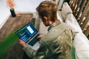 Dizüstü bilgisayarı olan genç bir adam, bir bilgisayara program kodu yazıyor, modern ofiste programcı olarak çalışıyor..