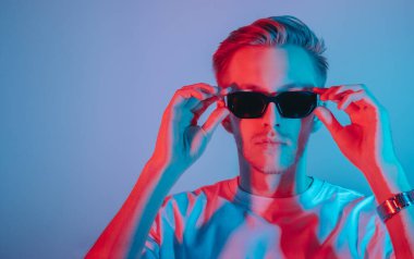 Moda portresi beyaz tişörtlü genç adam ve kırmızı ve mavi ışıklı siyah güneş gözlüğü..