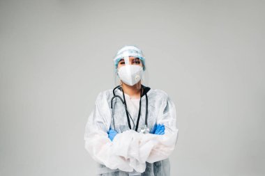 Tıbbi koruyucu maske, eldiven ve koruyucu giysi giyen genç hemşire kadın hastane çalışanı beyaz arka planda izole edilmiş ve fotokopi alanı var..