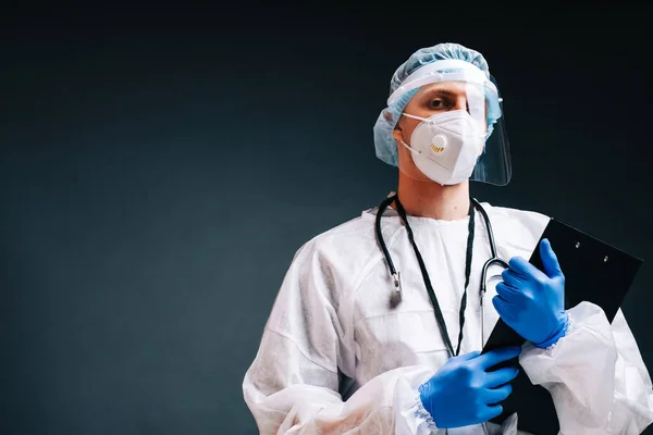 Young man nurse hospital worker in medical protective mask, gloves and protective wear isolated on dark background with copy space.