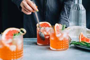 Kadın barmen taze limonata pişiriyor. Bardakta buzlu, greyfurtlu ve biberiyeli..