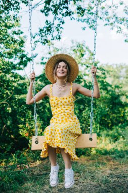 Açık havada hasır şapkalı çekici genç bir kadının portresi güneşli bir yaz gününde salıncakta.