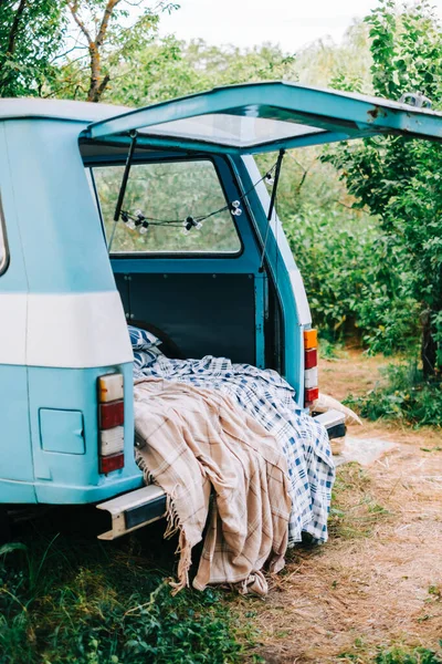 Blue-white retro van in nature, with cozy decorations, blanket and pillow, vacations in nature concept