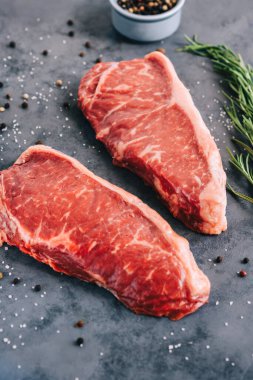 Çiğ New York bifteği. Gri arka planda, biberiye ve baharatlarla izole edilmiş.