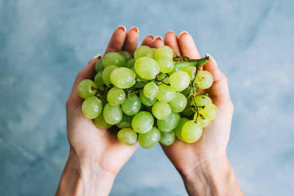 Зеленый спелый виноград в руках на синем фоне, крупным планом.