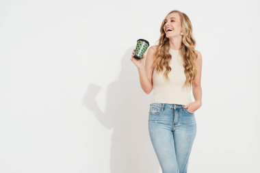 Beyaz duvarda gülümseyen genç sarışın kız cep telefonuyla kahve içiyor.