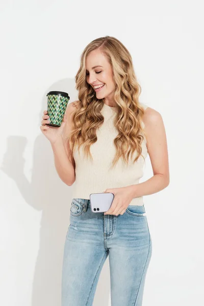 Joven Rubia Sonriente Una Pared Blanca Tomando Café Con Teléfono —  Fotos de Stock