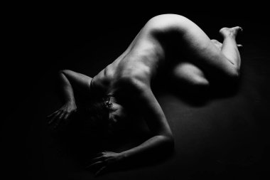 Yerde yatan çıplak bir kadının sanatsal siyah beyaz fotoğrafı.