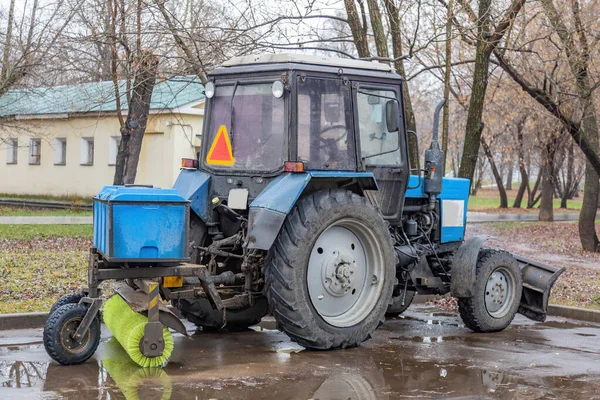 秋の街のぬれた通りで雪をきれいにするためのラドルとブルートラクター — ストック写真