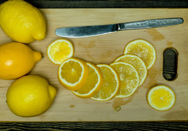 whole ripe lemons and halves of lemons with a knife on a cutting wooden board