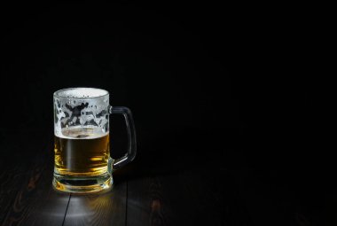 Hafif biralı cam bardak, koyu ahşap arka planda köpüklü yarı sarhoş.