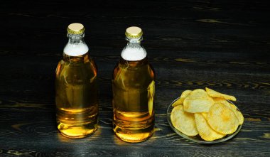 Köpüklü iki şişe light bira ve koyu ahşap arka planda küçük bir tabakta bir avuç cips.